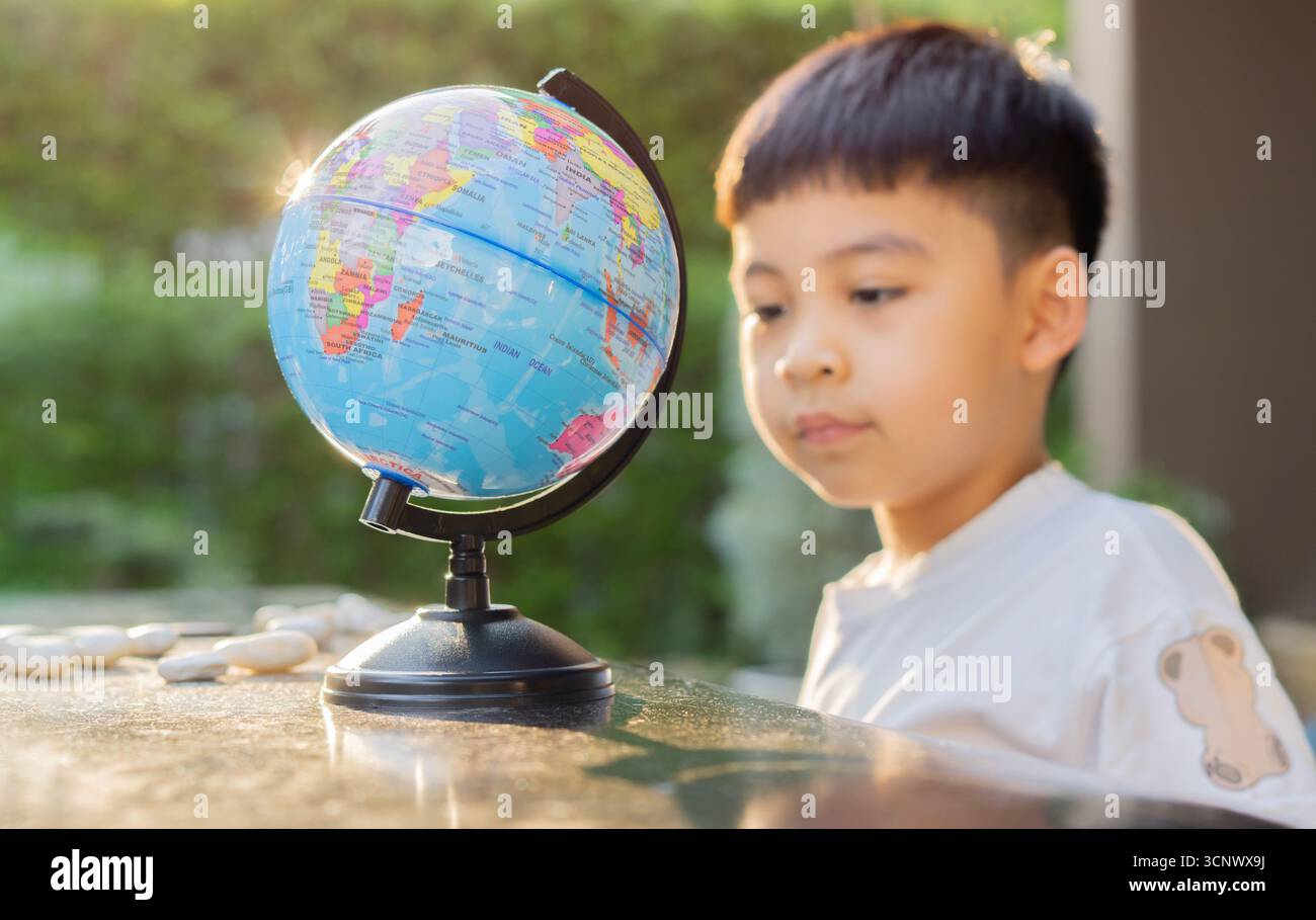 Happy Asian child boy looking at Globe global education world map while playing and joyfuling at outdoor. Kids Education concept. Selective focus. Stock Photo