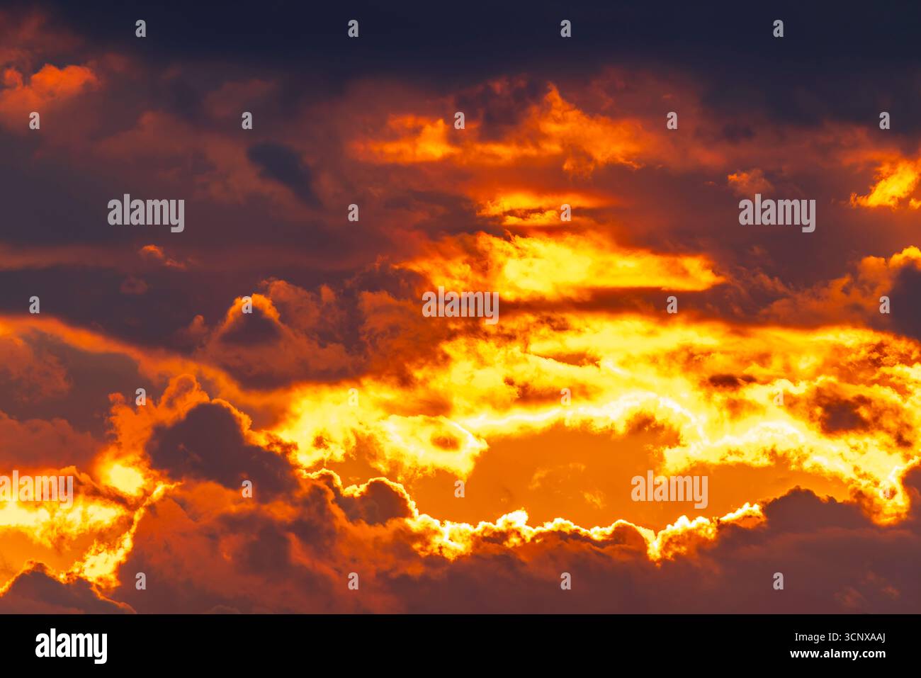 Intense golden and orange light bursts through dark dramatic clouds Stock Photo