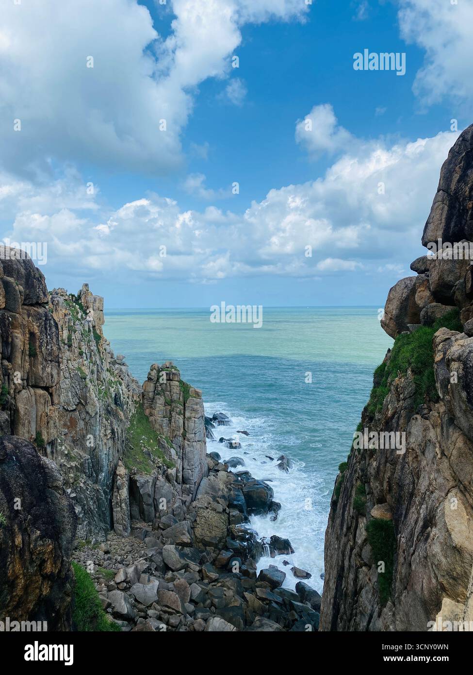 Sea view framed by rugged cliffs under a bright blue sky dotted with fluffy white clouds. - Smartphone Captured Stock Image