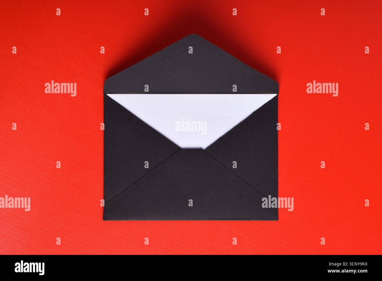 Opened black paper envelope with paper sheet isolated on red background Stock Photo