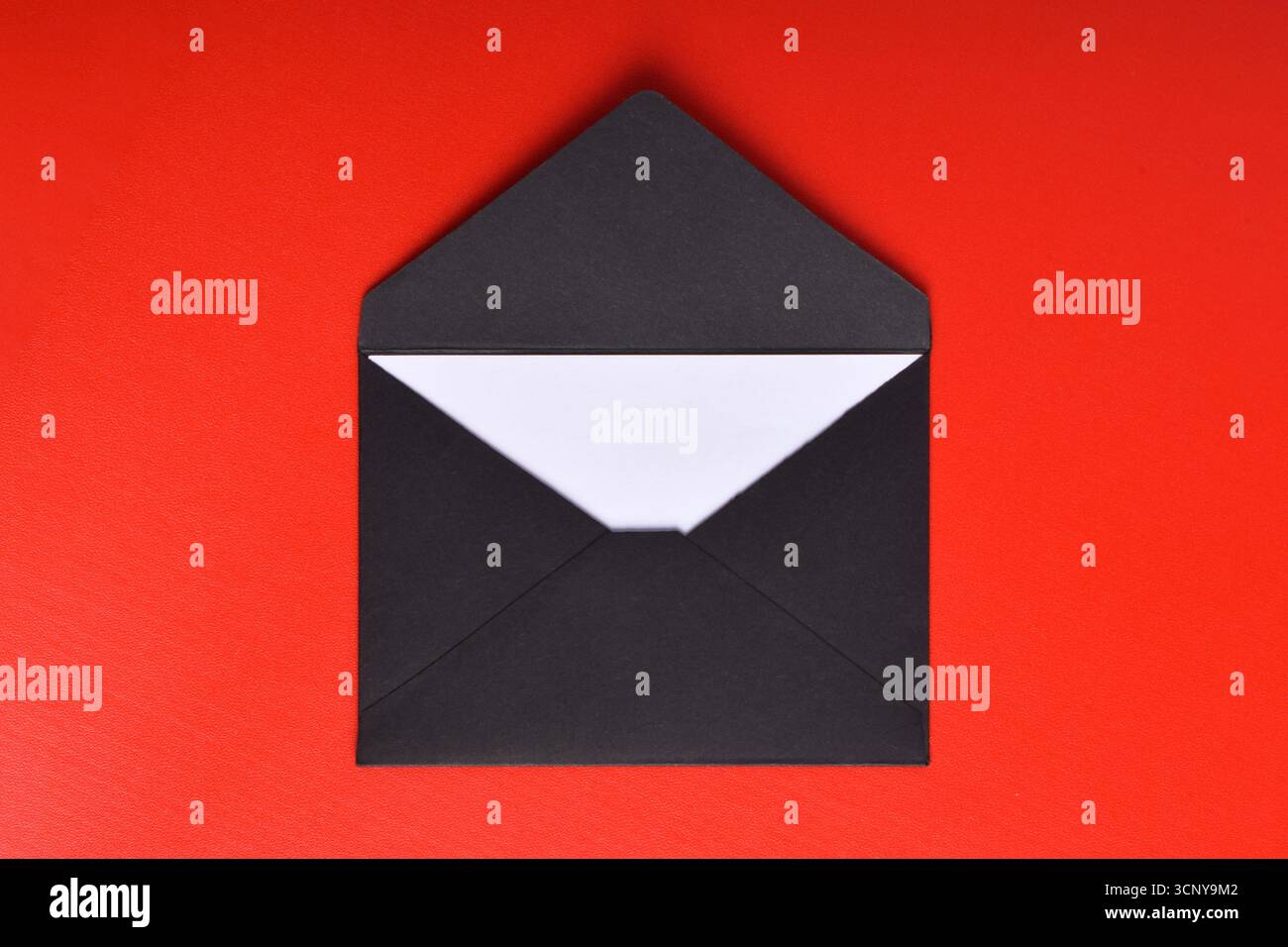 Opened black paper envelope with paper sheet isolated on red background Stock Photo