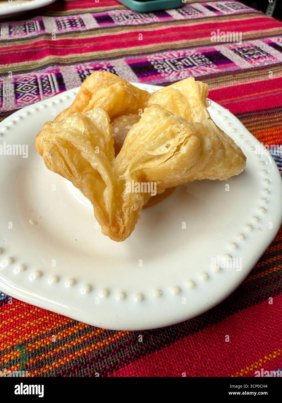Traditional Argentine fried pastry served on a white plate with a colorful woven tablecloth background in Buenos Aires, Argentina. - Smartphone Captured Stock Image