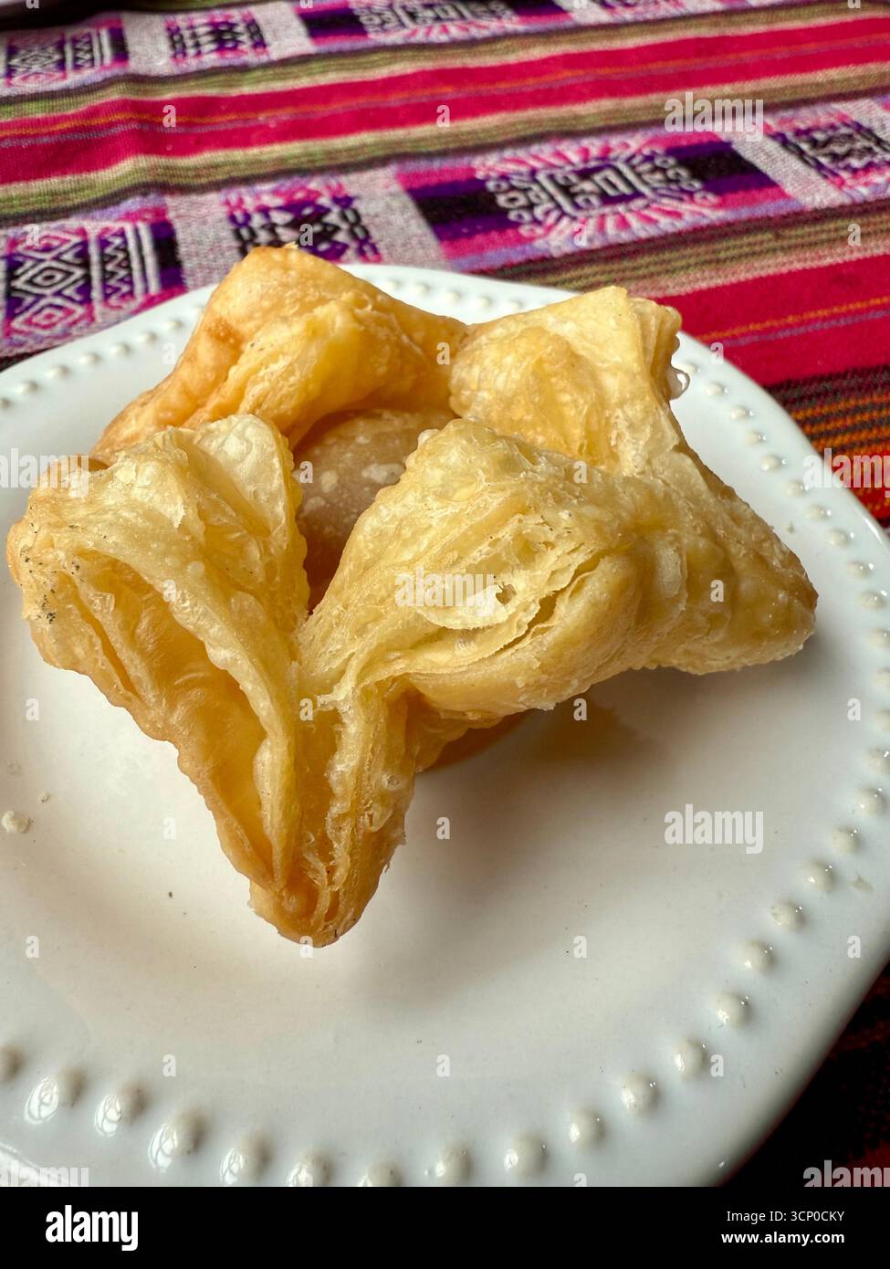 Traditional Argentine fried pastry served on a white plate with a colorful woven tablecloth background in Buenos Aires, Argentina. - Smartphone Captured Stock Image