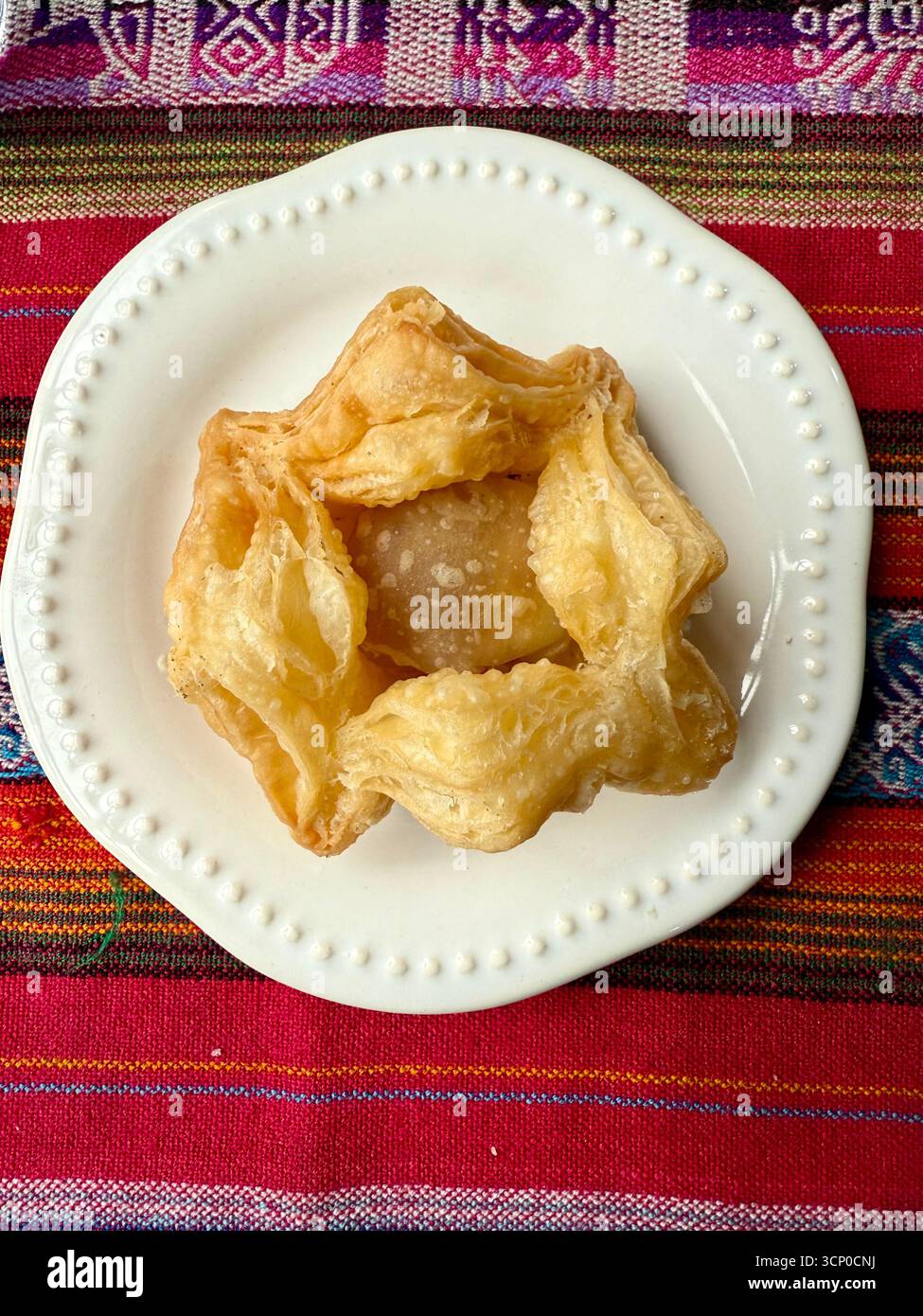 Traditional Argentine fried pastry served on a white plate with a colorful woven tablecloth background in Buenos Aires, Argentina. - Smartphone Captured Stock Image