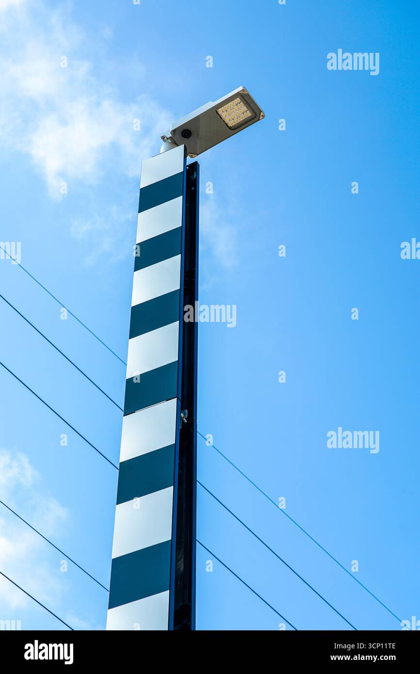 Modern LED street light with vertical black and white reflective panels against a clear blue sky and power lines background Stock Photo