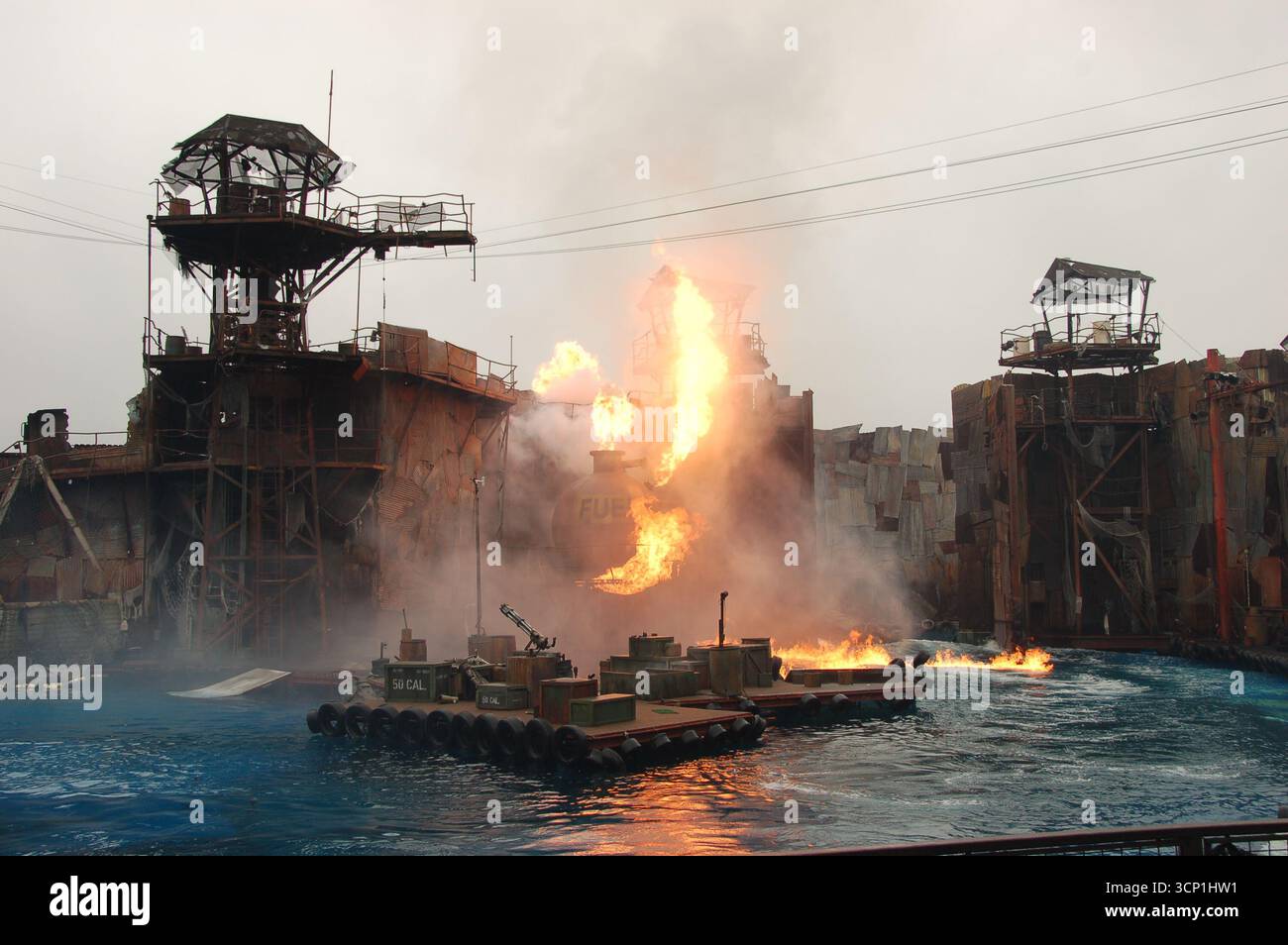 Dramatic explosion during the WaterWorld live show at Universal Studios Hollywood, with towering flames, smoke, and set structures over the water stag Stock Photo