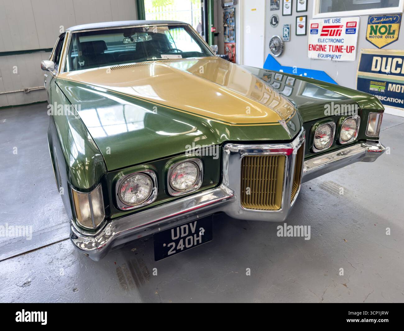 Classic green and gold vintage 1970s Pontiac Grand Prix car displayed in a garage with automotive posters and a polished concrete floor - Smartphone Captured Stock Image