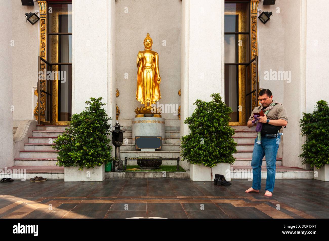 Man barefoot using phone at buddhist shrine in Thailand Stock Photo