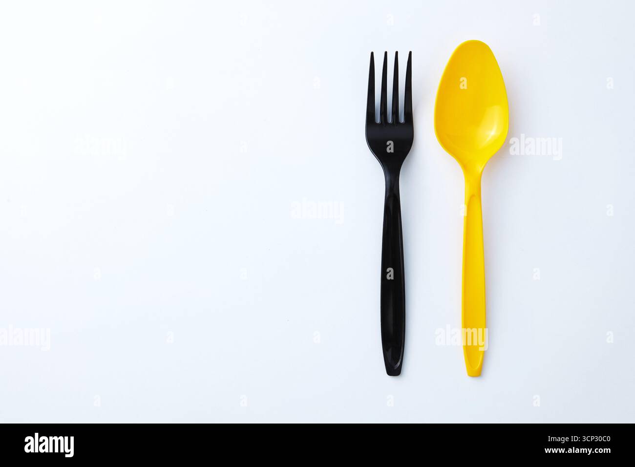 A black plastic fork next to a yellow plastic spoon on a white background Stock Photo