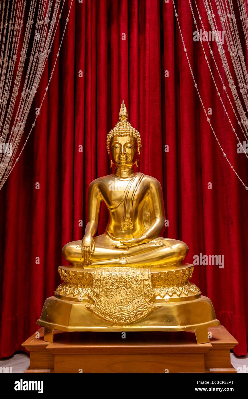 A golden Buddha image in the meditation posture, subduing Mara, against a red curtain at Wat Tha Sung. Stock Photo