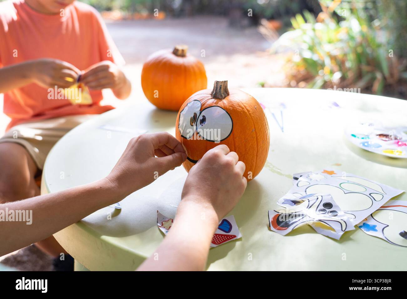 Children's hands applying face stickers to a pumpkin, creating a funny character for halloween Stock Photo