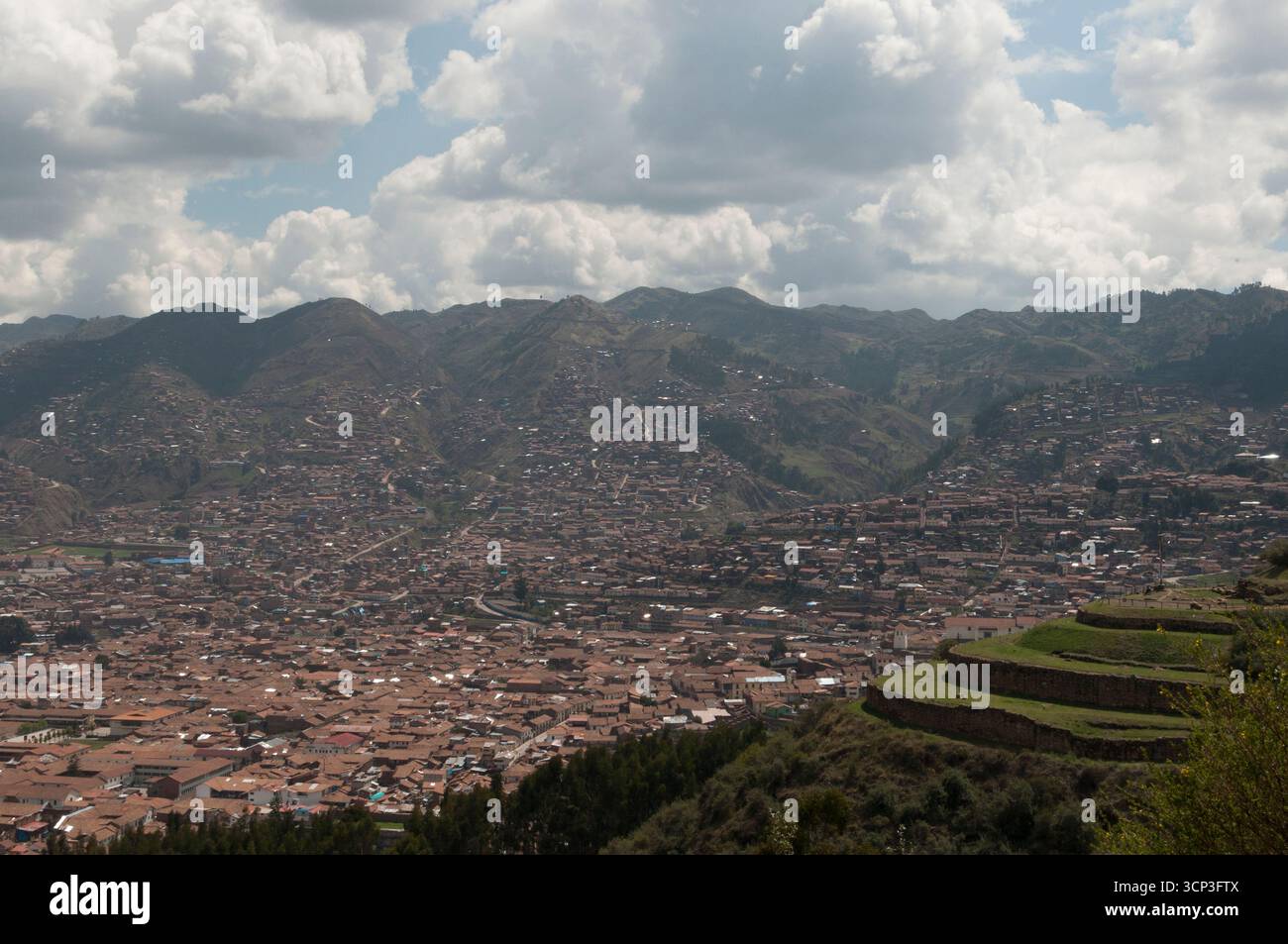 Ruinas y muro de piedra en Sacsayhuamán, fortaleza inca en Cusco. Vista de Cuzco y de las bancadas del terreno cubiertas de vegetacion verde y nubes Stock Photo