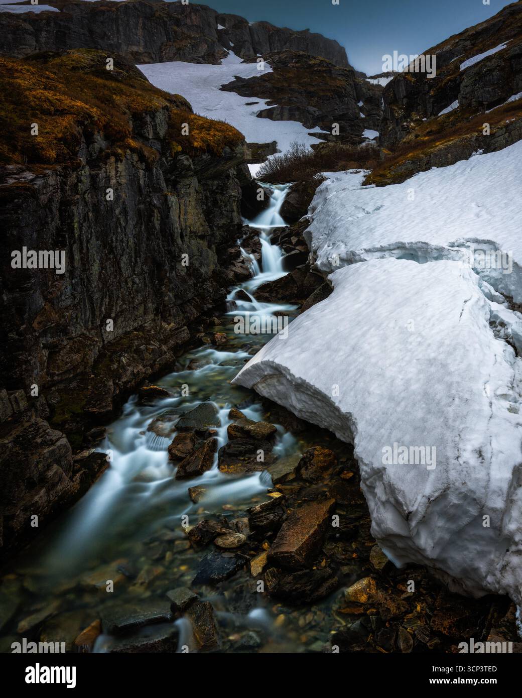 A waterfall cascades down from the snowy peaks of Norway’s highlands Stock Photo