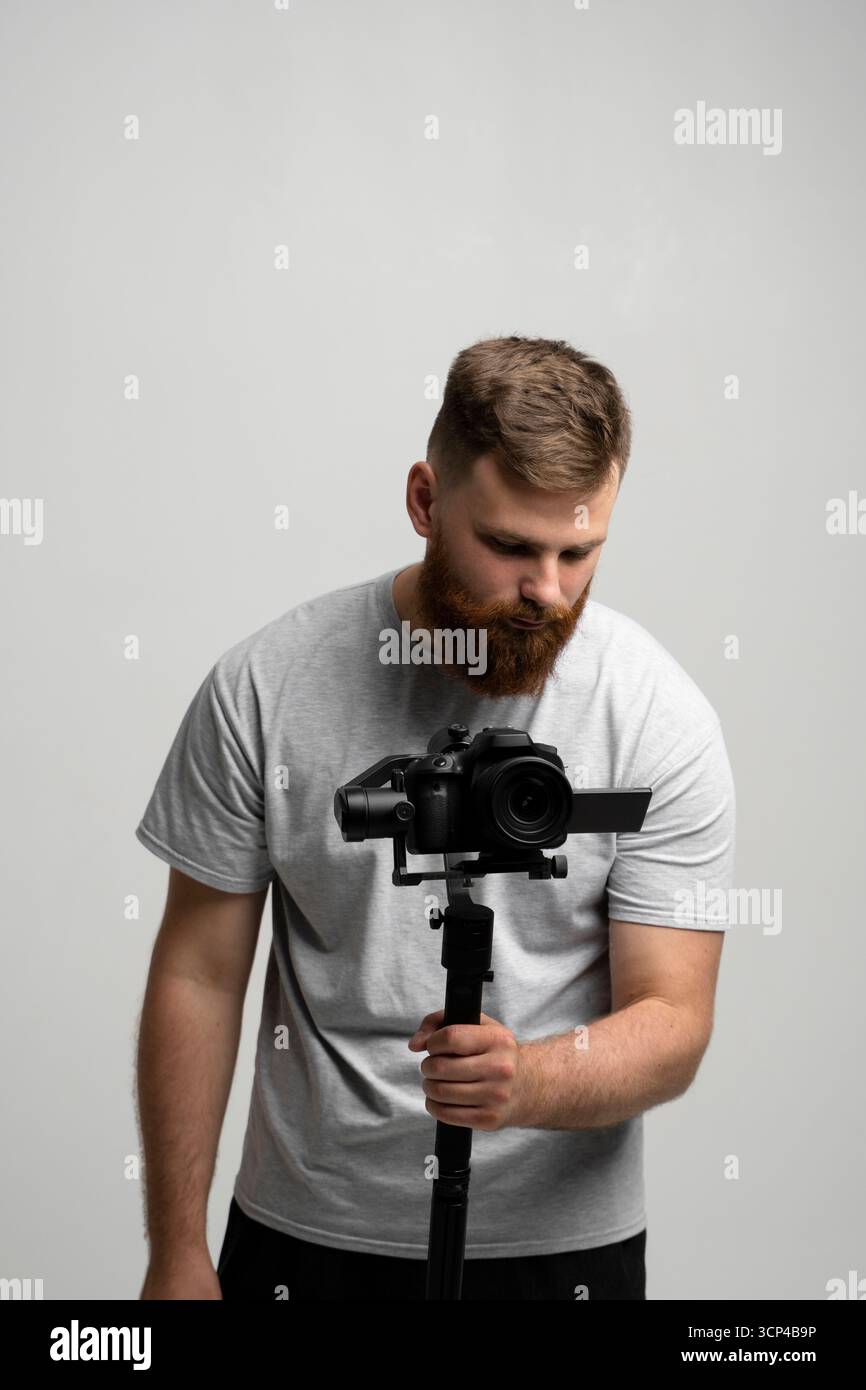 Bearded man using professional camera with stabilizer against grey background Stock Photo