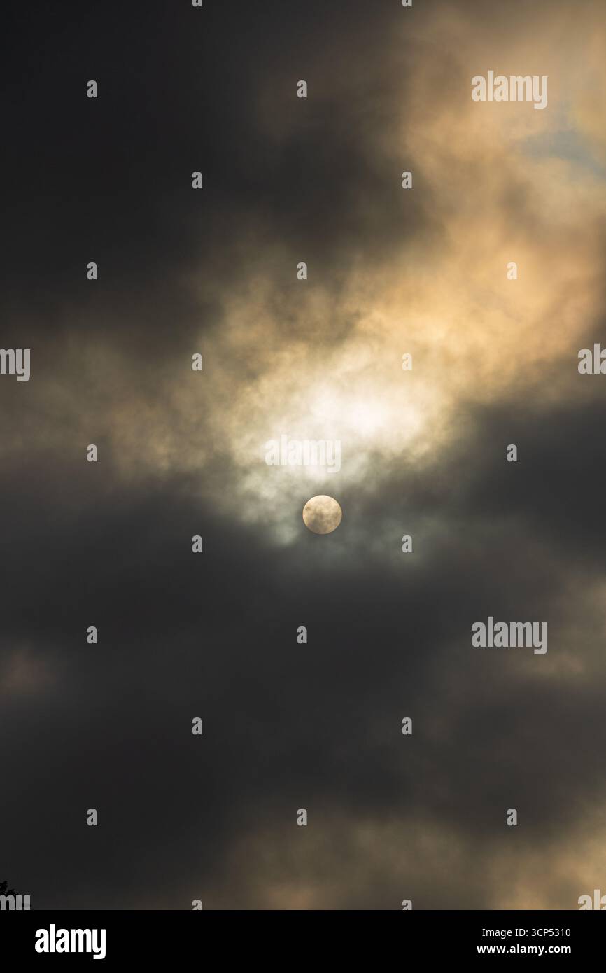dramatic sky with sun partially hidden by clouds Stock Photo