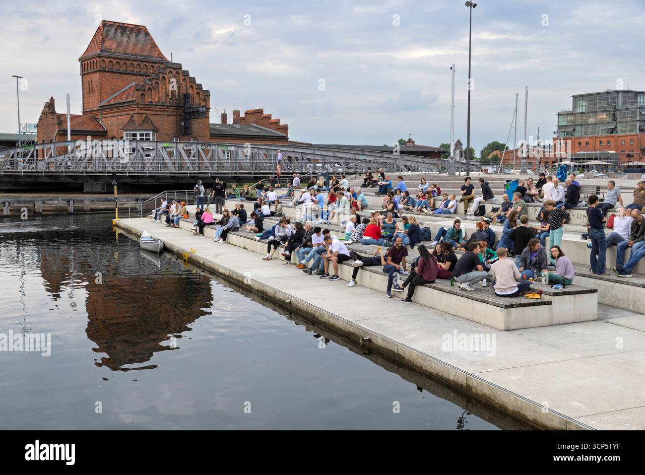 People sitting on the water stairs by the canal in the evening, Lubeck, Schleswig-Holstein, Germany, Europe Stock Photo
