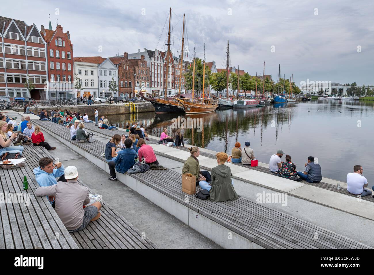 People sitting on the water stairs by the canal in the evening, Lubeck, Schleswig-Holstein, Germany, Europe Stock Photo