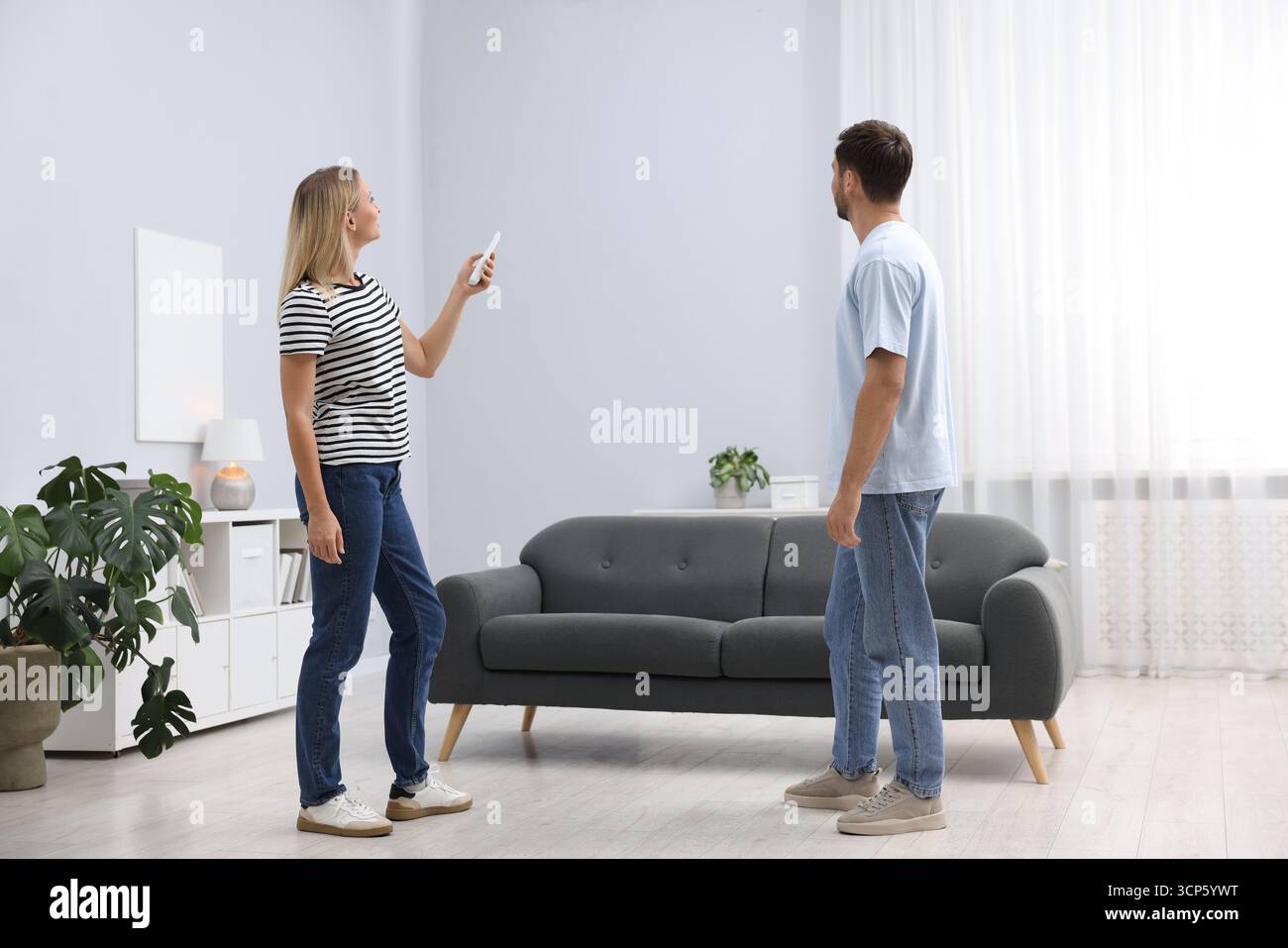 Couple using remote to control air conditioner at home Stock Photo