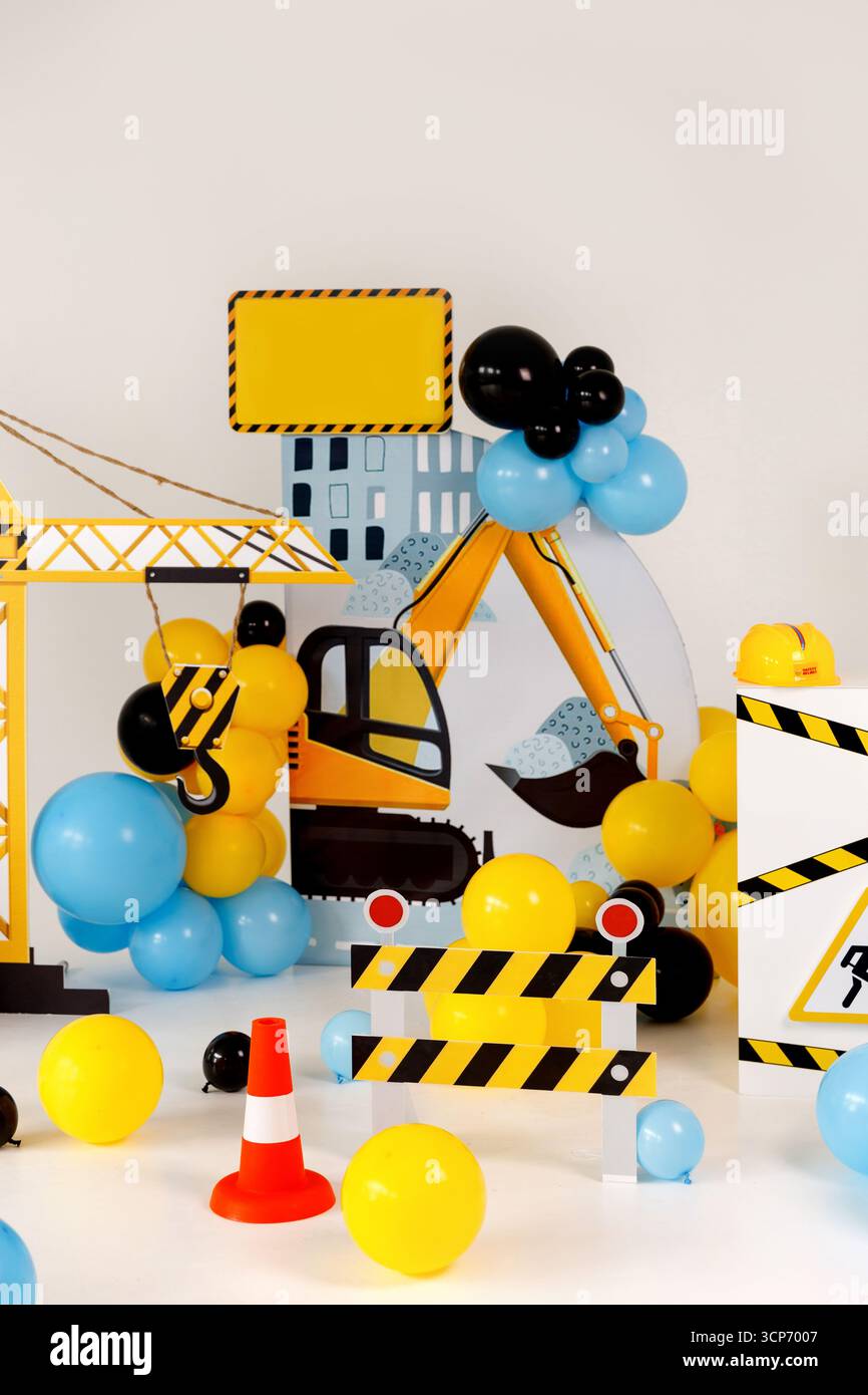 Playful construction zone decoration featuring toy excavator cutout, crane hook, striped barricade, caution tape, orange traffic cones, and colorful b Stock Photo