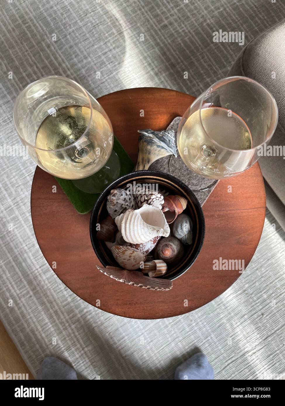 down view of two glasses of wine, a small bowl with sea shells, on a round wood table with a grey background - Smartphone Captured Stock Image