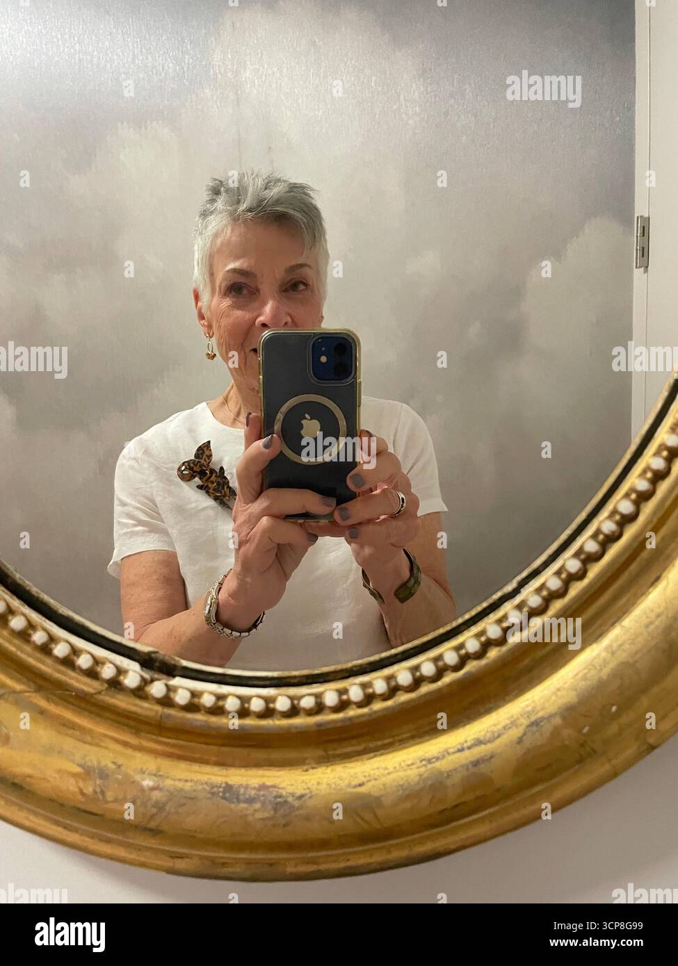 Middle aged woman with grey hair looking into a mirror while taking a selfie - Smartphone Captured Stock Image