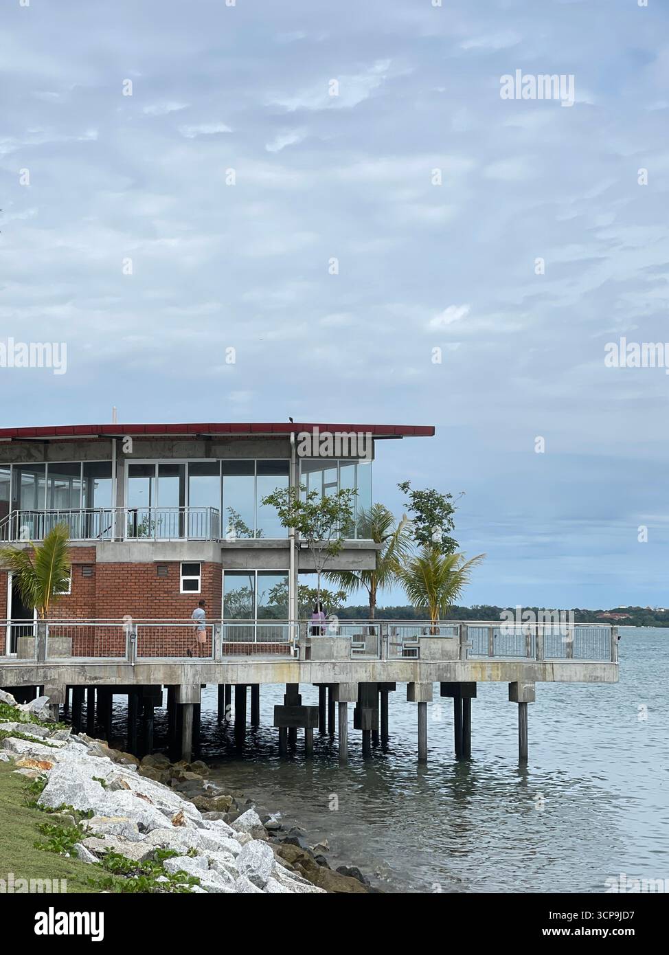 Port Dickson, Malaysia - September 15, 2025: Modern stilted building above calm water at PD Waterfront, with rocky white shoreline and blue ocean. - Smartphone Captured Stock Image