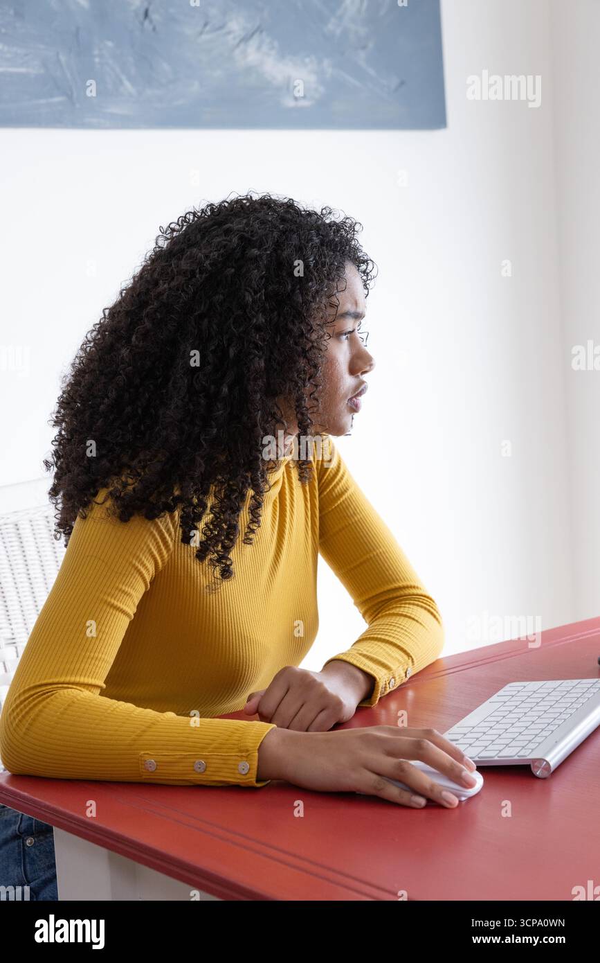 African american woman sitting at desk in home office using computer mouse under painting Stock Photo