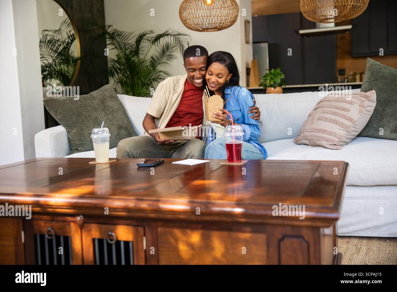 African American couple hugging and sharing takeout in home living room ...