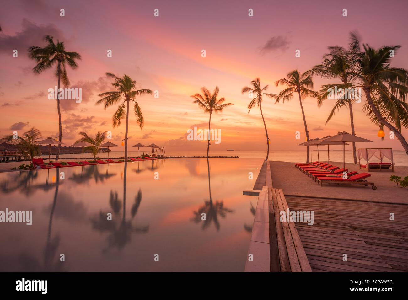 Amazing sunset pool palm trees and umbrellas reflecting in water, majestic tropical scene, summer vacation holiday mood, carefree relaxation leisure Stock Photo