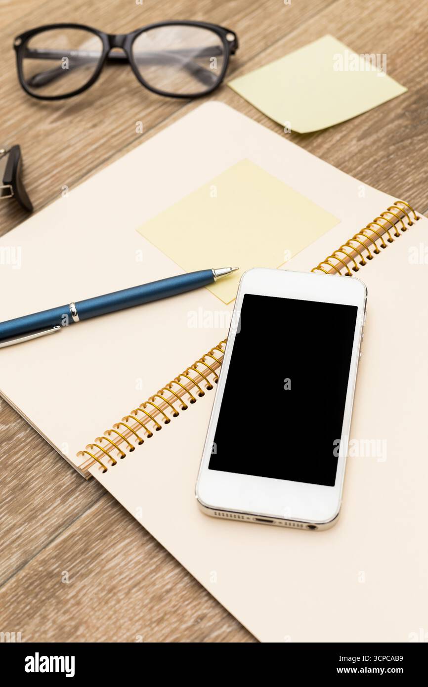 Workspace setup with notebook, pen, smartphone, and glasses during a creative session Stock Photo