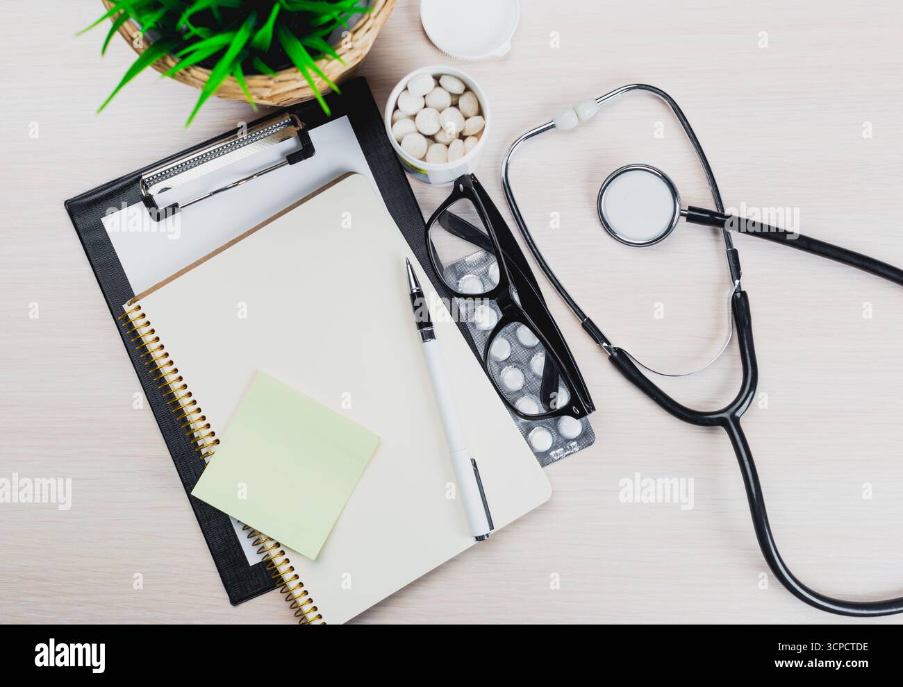Medical workspace with stethoscope, notepad, and medications arranged on a light wooden table Stock Photo