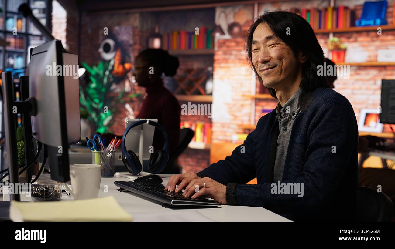 Portrait of smiling senior engineer coding advanced AI algorithm in startup office, refining machine learning models. Cheerful man using coding platform in Silicon Valley workplace, camera B Stock Photo