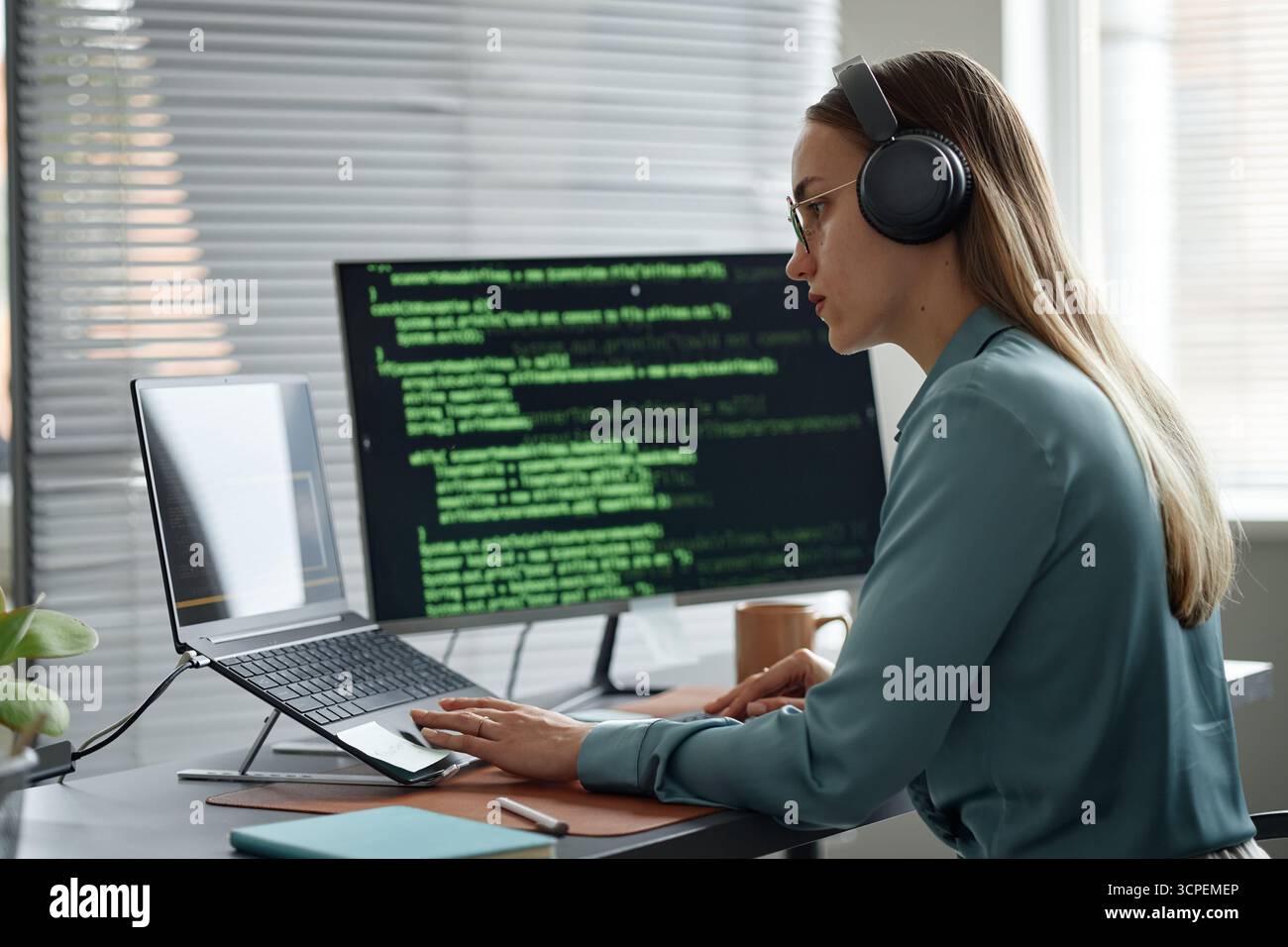 Young Adult Woman Writing Code on Laptop While Wearing Headphones Stock Photo