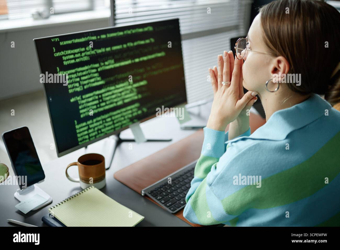 Young Woman Analyzing Code on Computer Monitor in Modern Office Stock Photo