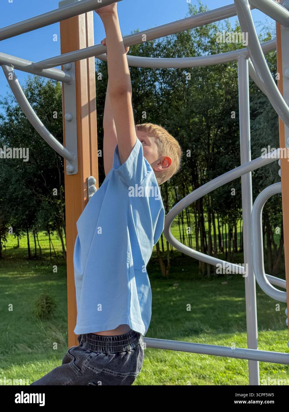 Teen boy working out on pull-up bars at an outdoor sports playground during a bright summer day, fitness and activity concept - Smartphone Captured Stock Image