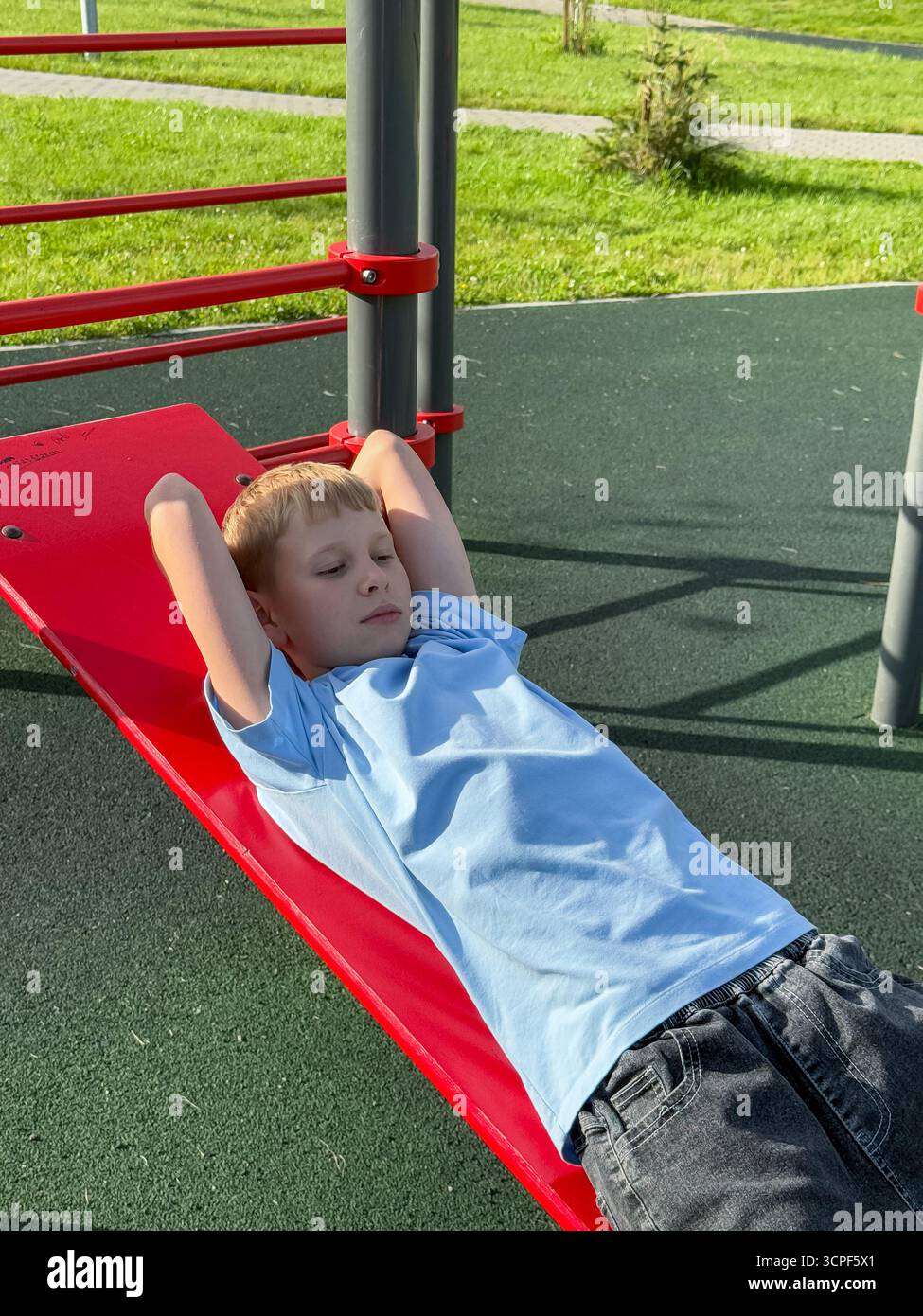 Teen boy exercising on pull-up bars at an outdoor sports playground on a sunny summer day, fitness and athletic activity concept - Smartphone Captured Stock Image