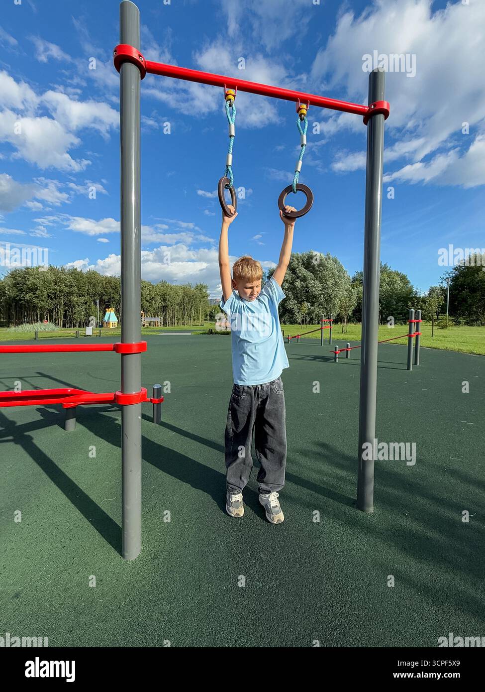 Teen boy exercising on gymnastic rings at an outdoor sports playground during a bright summer day, fitness and athletic activity concept - Smartphone Captured Stock Image