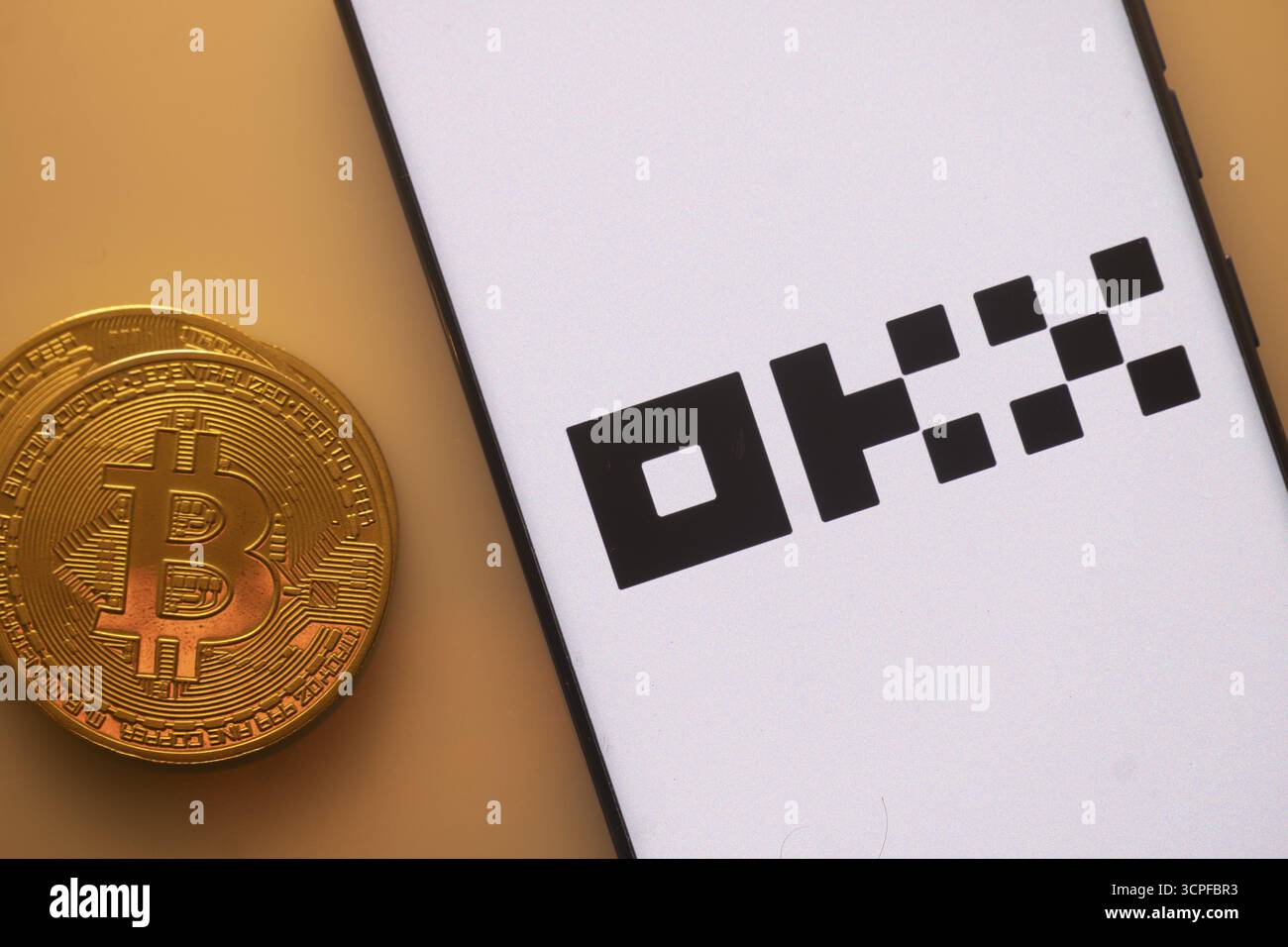 A Bitcoin and OKX logo on a white screen with black text Stock Photo