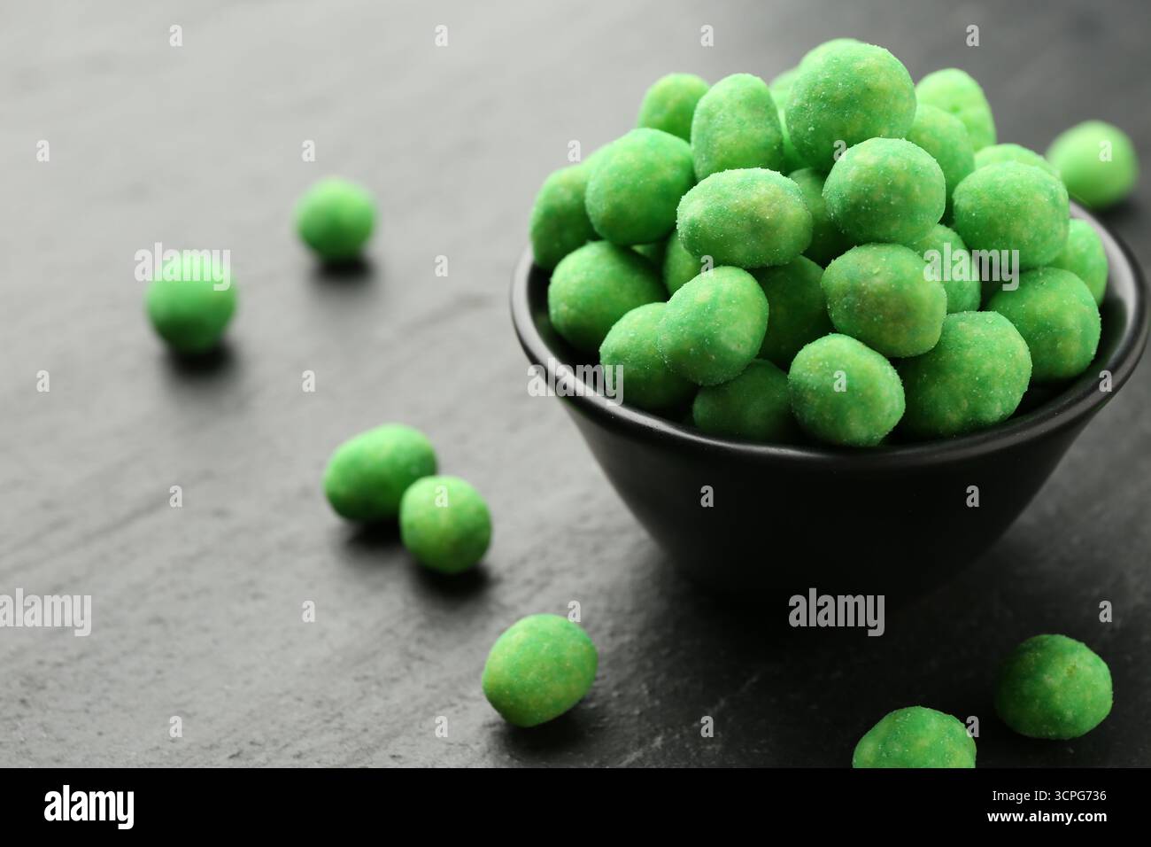 Delicious wasabi coated peanuts and bowl on dark textured table, closeup Stock Photo