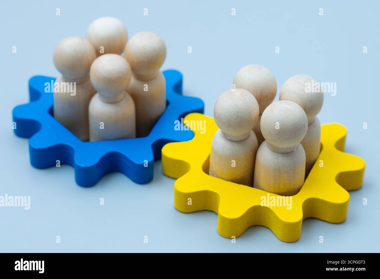 Wooden human figures inside blue and yellow gear shapes. Mergers and acquisitions, teamwork, integration, and corporate collaboration concepts. Stock Photo