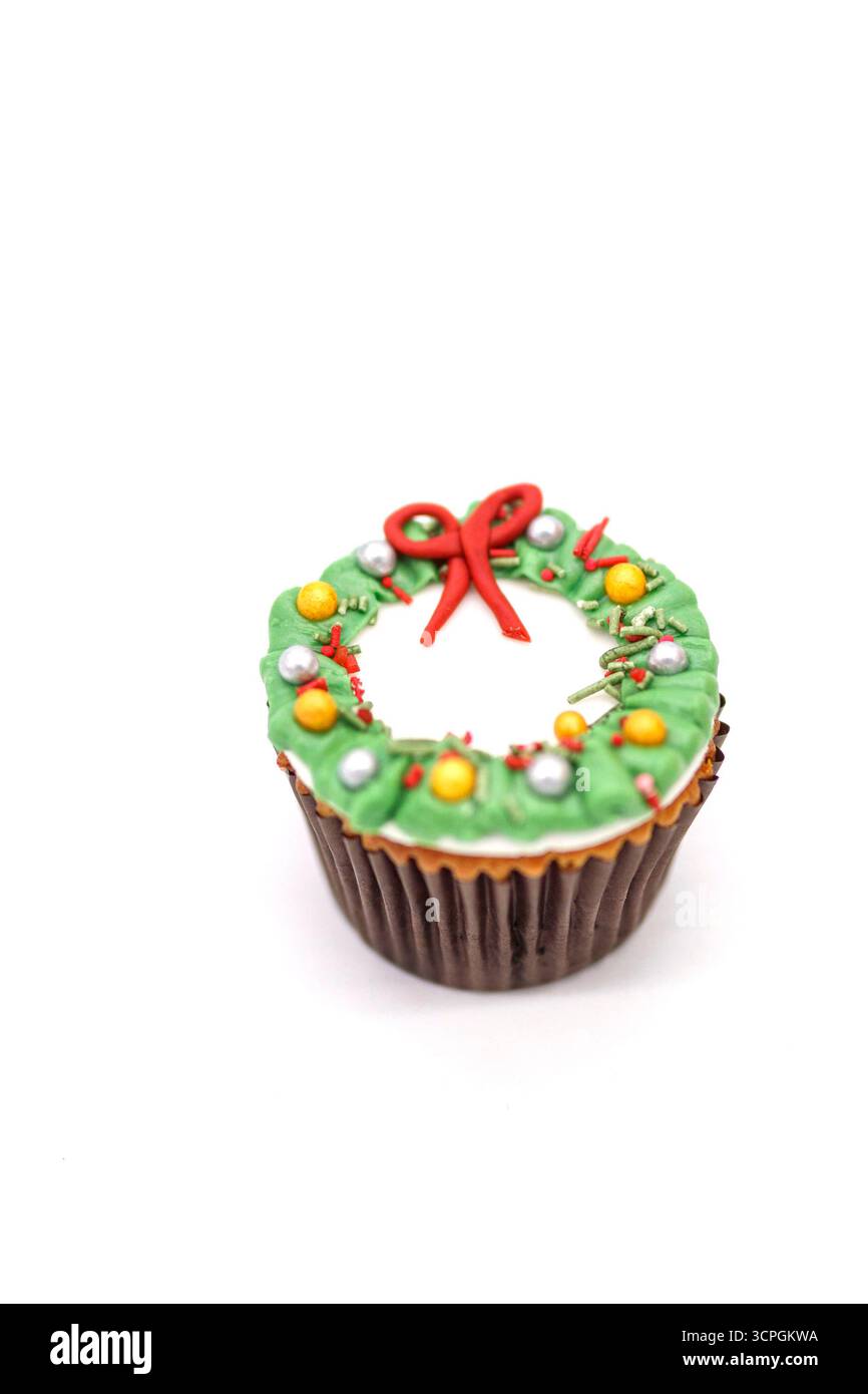 Chocolate cupcake decorated with green frosting in the shape of a holiday wreath featuring a red bow and colorful decorations Stock Photo