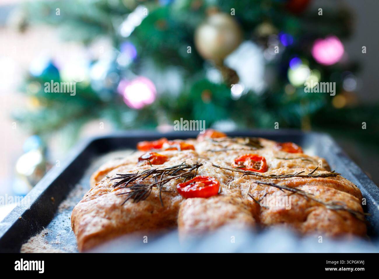 Fresh homemade focaccia bread on a baking tray in front of a decorated Christmas tree with colorful ornaments Stock Photo