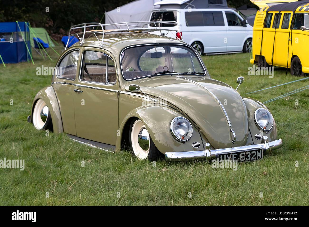 Vintage lowered slammed  grey green Type 1 Volkswagen Beetle in a field at a car show with other classic cars and tents in the background Stock Photo