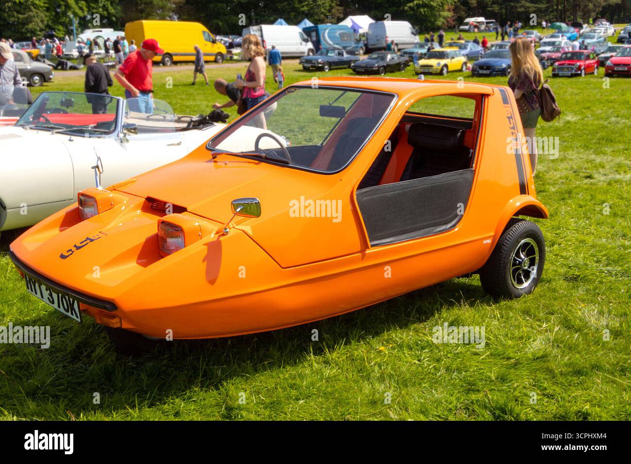 Bright orange vintage Bond Bug three-wheeler car on display at an outdoor car show with people mingling in the background uk Stock Photo