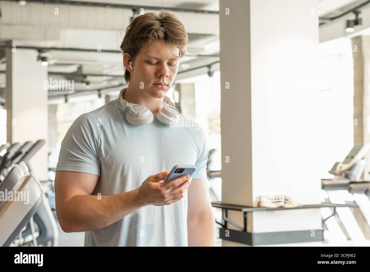 Athlete man with mobile phone standing at gym. Warming up. Preparation for cardio training. Trainer waiting for client. Close up. Stock Photo