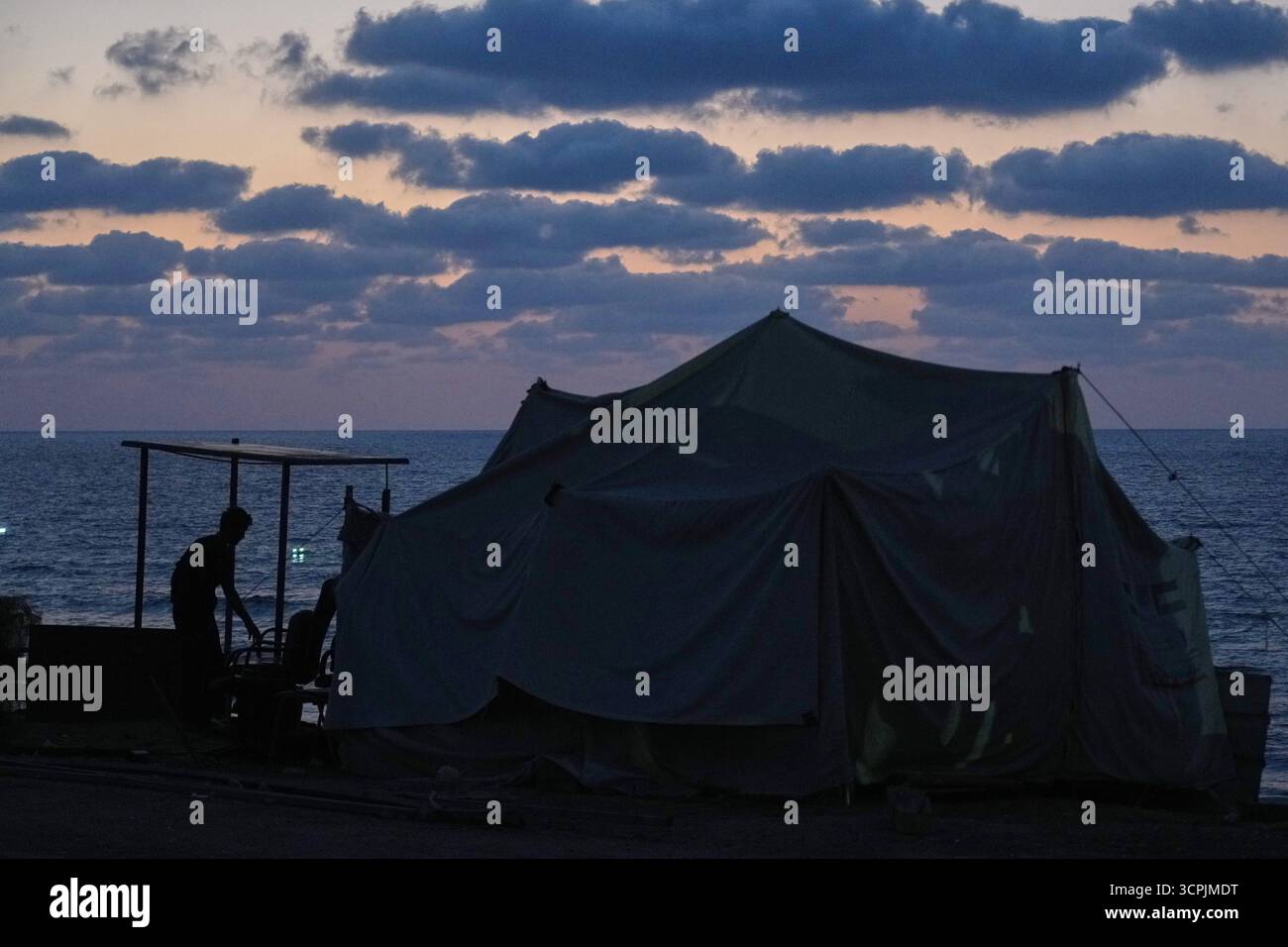 A displaced Palestinian stands next to a tent set up on the seafront ...