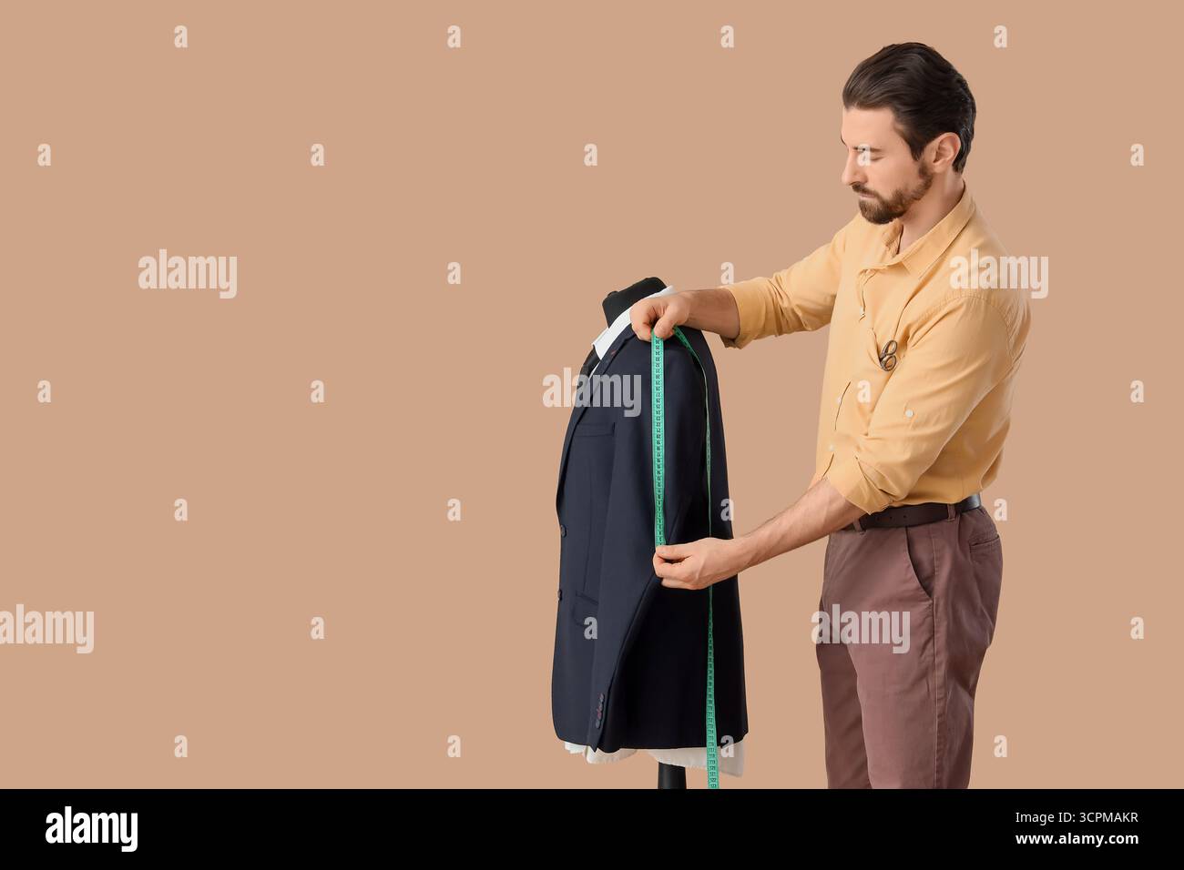 Male tailor measuring jacket on beige background Stock Photo
