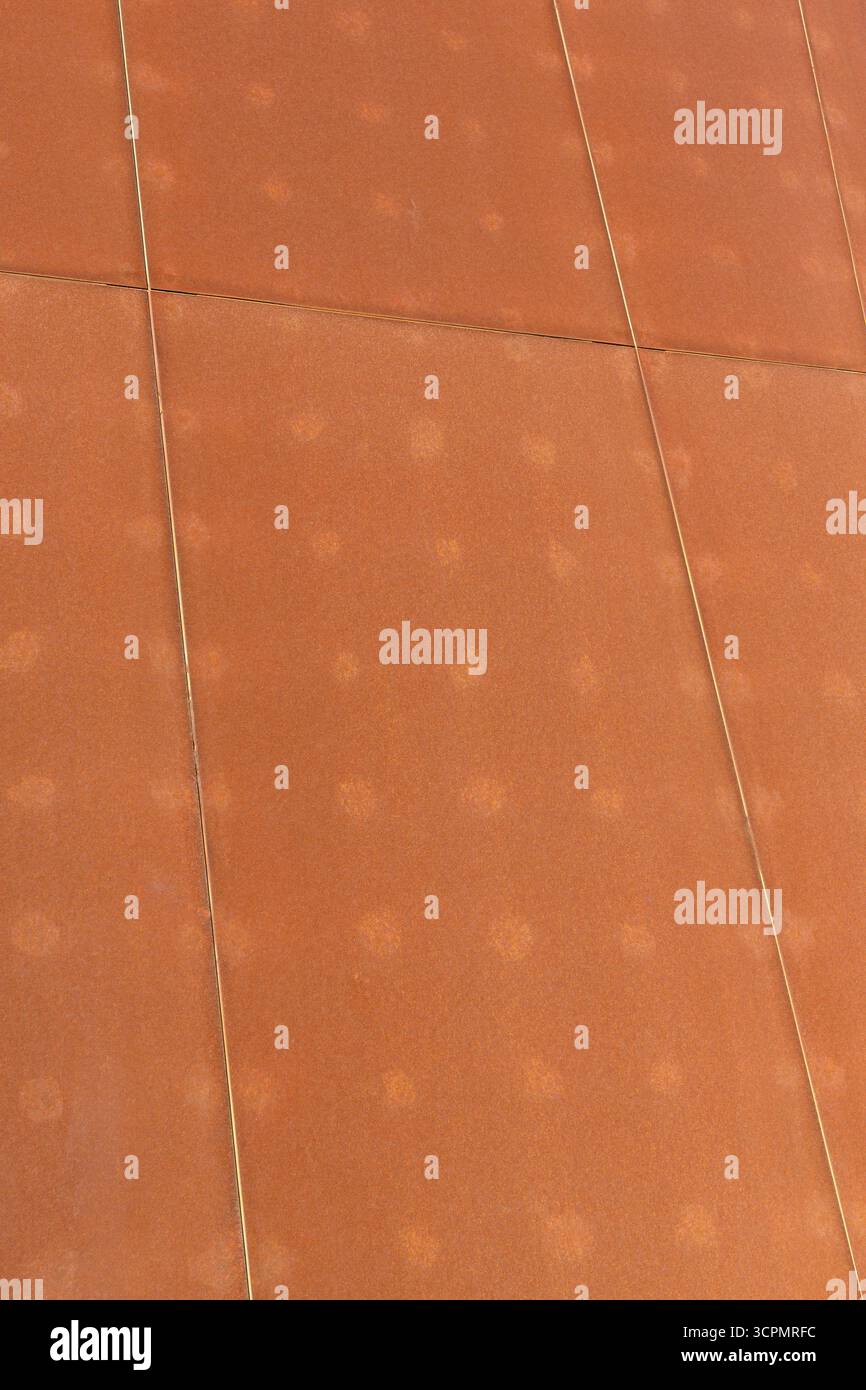 Rust-colored steel plate wall with a weathered texture, arranged in a large panel pattern. Stock Photo