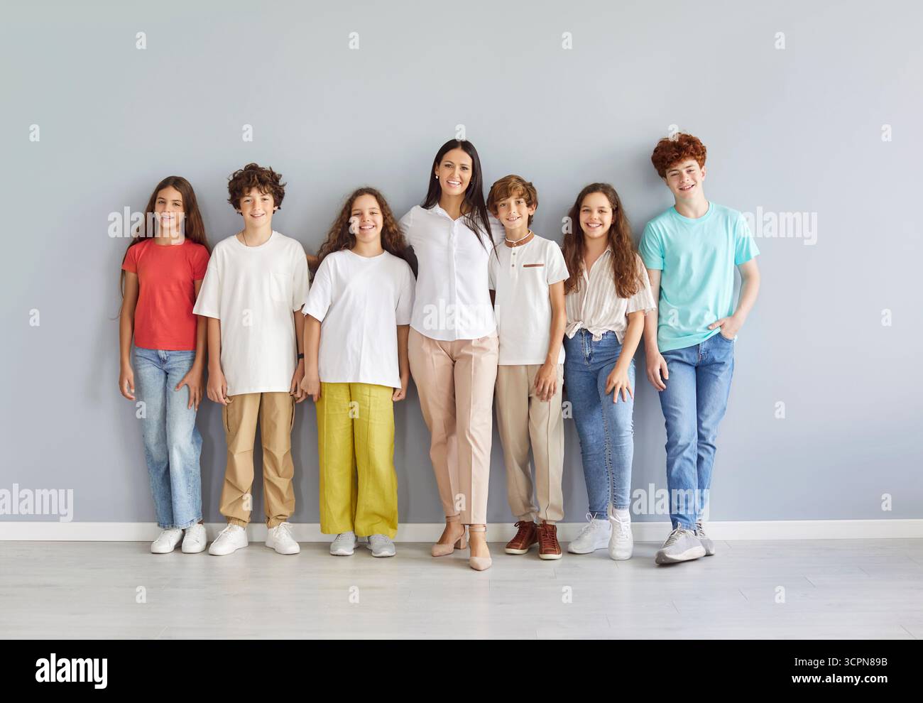 Portrait Of Happy Teacher And Group Of Students Standing On Grey Background Stock Photo