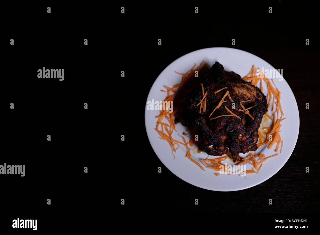 Overhead View of Darkly Spiced Roasted Meat or Tandoori Chicken on a White Plate Stock Photo